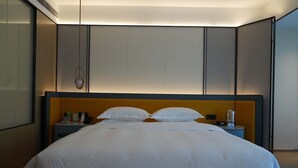 A neatly made bed with white linens, a wooden headboard, and a bedside table with a lamp and a phone. - XUANDE GATE HOTEL (Jiaxing)