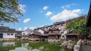 A traditional courtyard with a pond, stone balustrade, and traditional buildings with tiled roofs. - XUANDE GATE HOTEL (Jiaxing)
