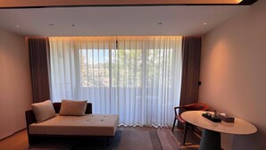 A modern hotel room with a sofa, a small table, and a view through sheer curtains. - XUANDE GATE HOTEL (Jiaxing)