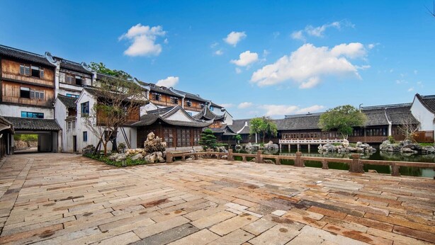 A traditional courtyard with stone paving, wooden buildings with tiled roofs, and a small water feature. - XUANDE GATE HOTEL (Jiaxing)