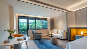 A modern hotel room with a large window, a sofa, a dining table, and a small side table. - XUANDE GATE HOTEL (Jiaxing)