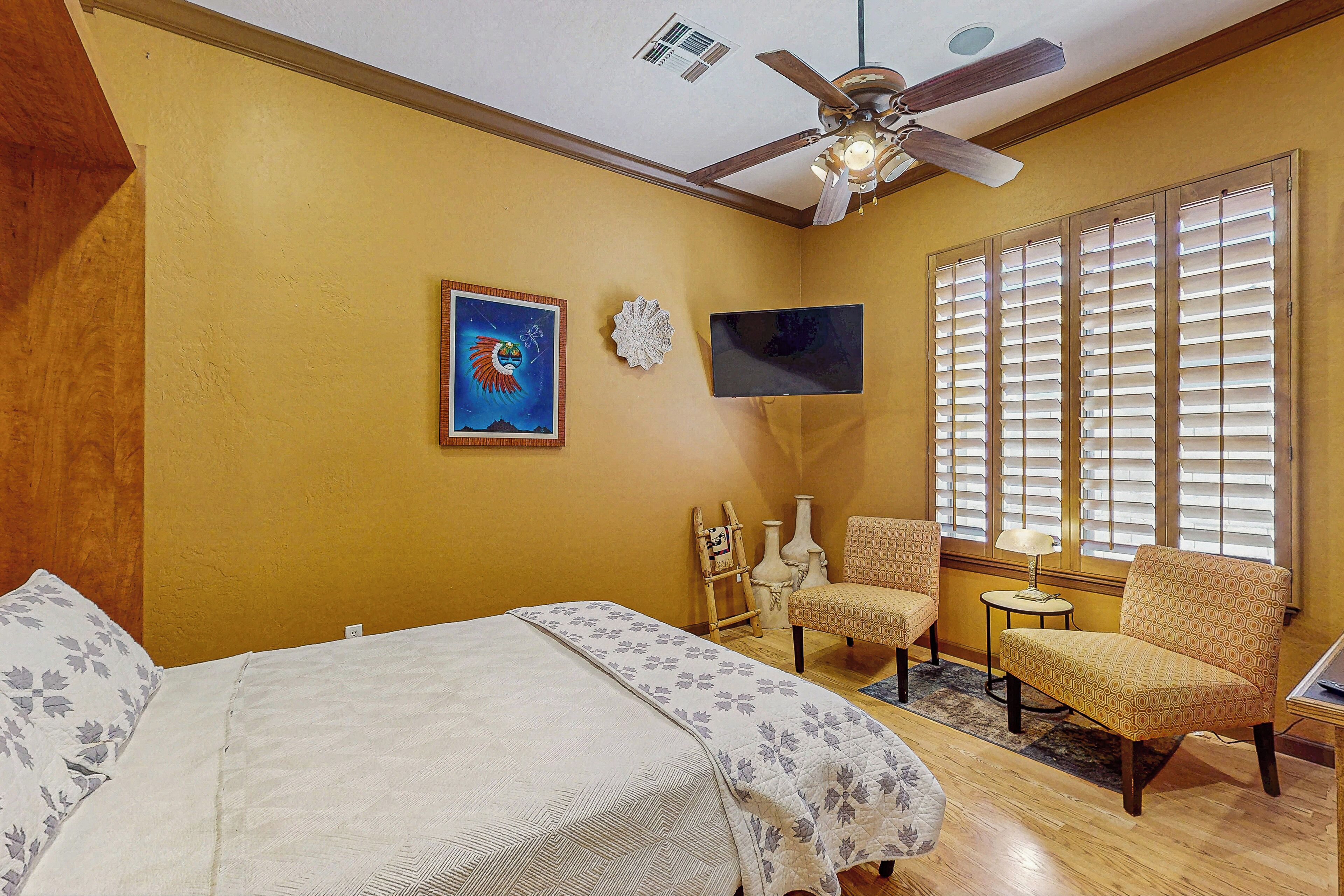 A bedroom with a bed, a chair, a TV, and a window with blinds.