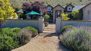 A gated entrance to a residential property with a gravel driveway, surrounded by well-maintained hedges and flowering plants. - Mountain-View Backyard Oasis! King City Getaway (King City)