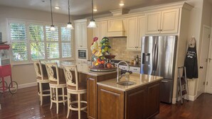 A kitchen with wooden cabinets, a stainless steel refrigerator, and a central island with bar stools. - Mountain-View Backyard Oasis! King City Getaway (King City)