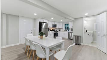 Une cuisine moderne avec des meubles blancs, des appareils en acier inoxydable et un coin repas comprenant une table et des chaises blanches.