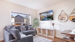 Un soggiorno moderno con un divano grigio, un tavolo consolle in legno e un quadro che raffigura un paesaggio montano.