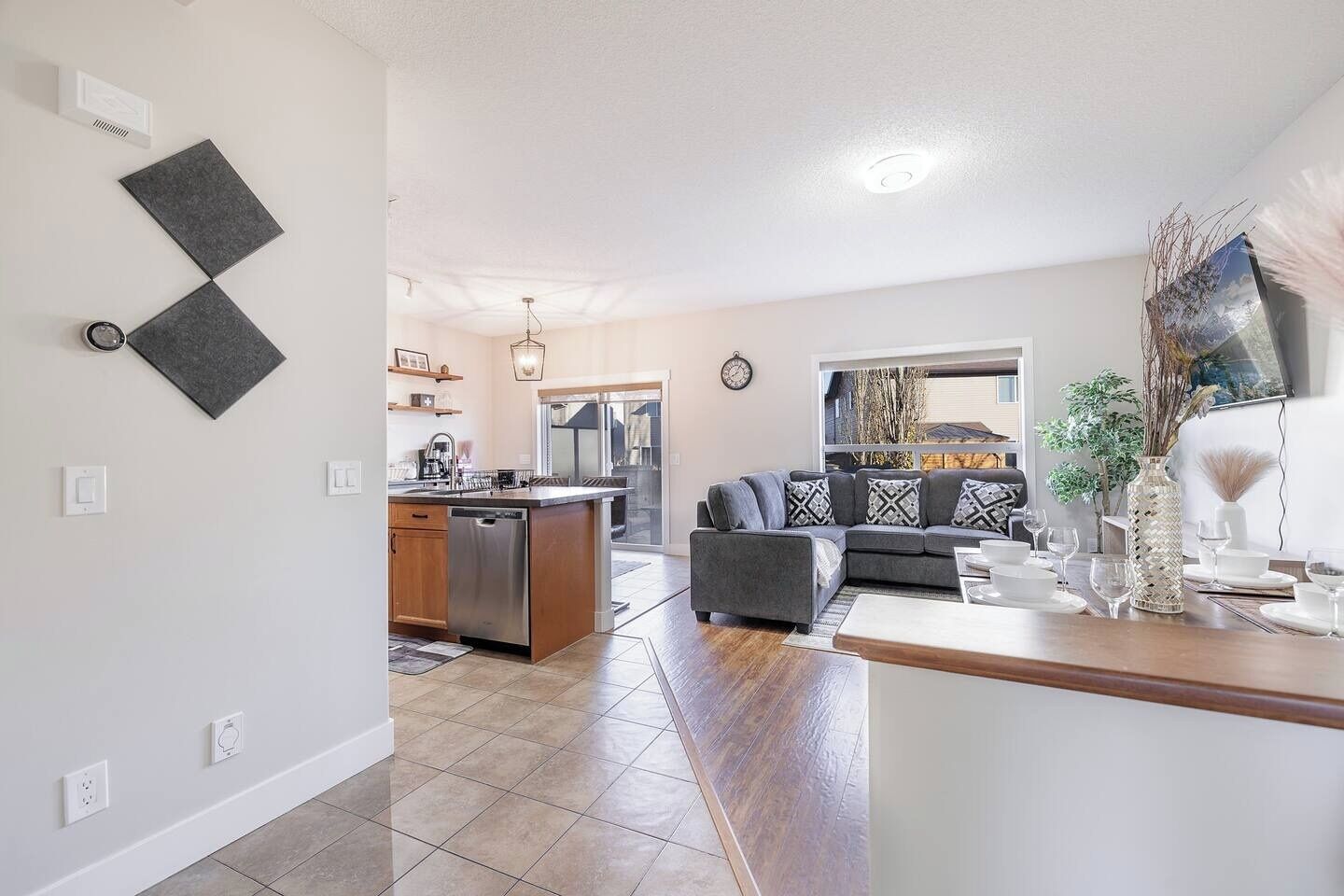 A modern kitchen with a central island, a dining area with a wooden table, and a living room with a sofa and decorative items.