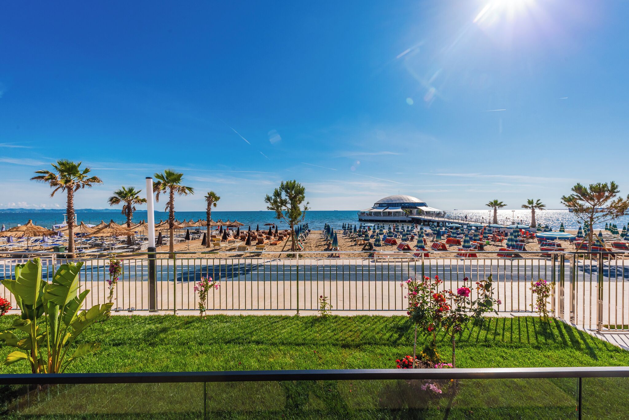 A beachside view with a pool area, palm trees, and a large building with a dome.