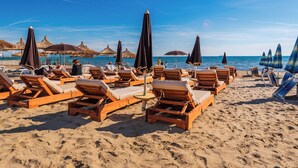 Une plage avec des chaises longues en bois et des parasols en chaume.