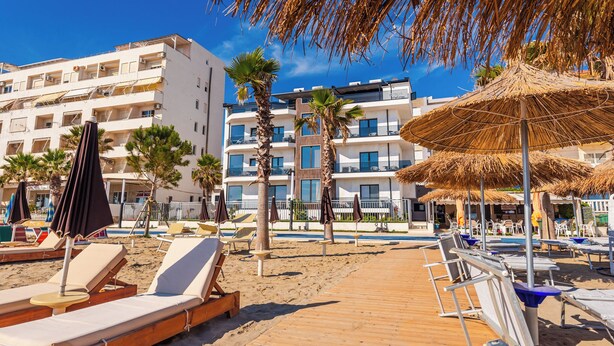 Un hôtel situé en bord de mer, doté de chaises longues, de parasols et d’une promenade en bois.