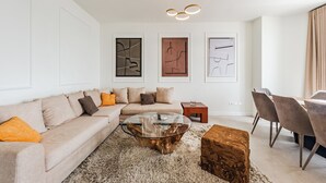 Un salon moderne avec un canapé beige, une table basse en verre et des œuvres d’art abstraites accrochées au mur.