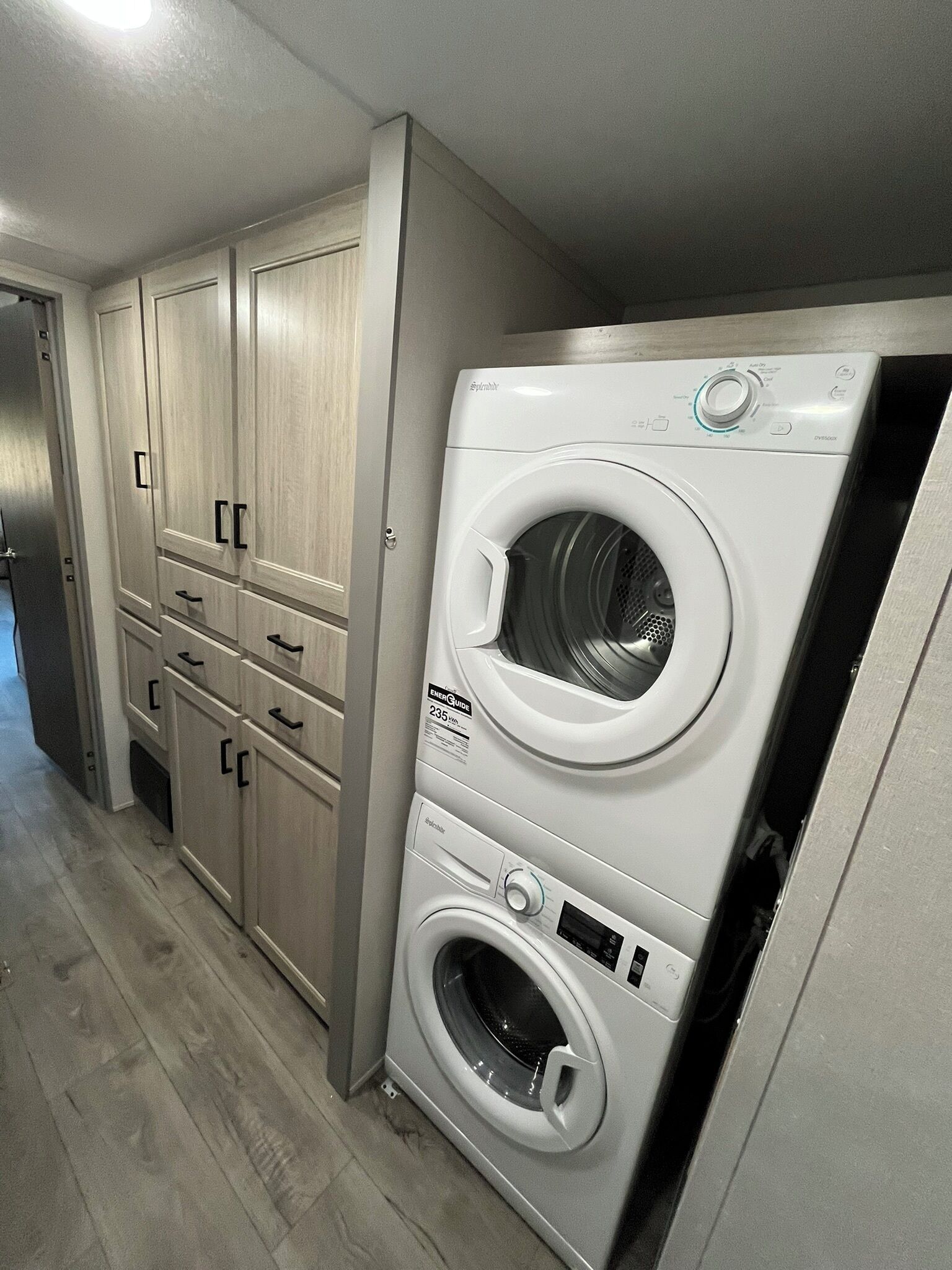 A laundry room with a front-loading washer and dryer, wooden cabinets, and a tiled floor.