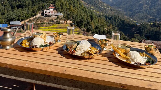 Een gedekte tafel met traditioneel eten en drinken, met uitzicht op een bergachtig landschap onder een heldere lucht.