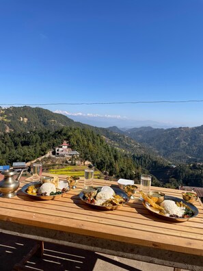 A table set with traditional food and drinks, overlooking a mountainous landscape with a clear sky. - Lekali Home & Organic Farmstay  (Dhunkharka)