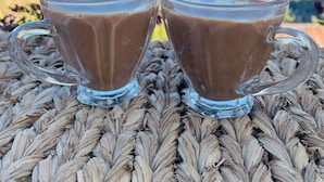 Twee glazen bekers warme chocolademelk op een geweven mat, met een mooi uitzicht op de bergen op de achtergrond.