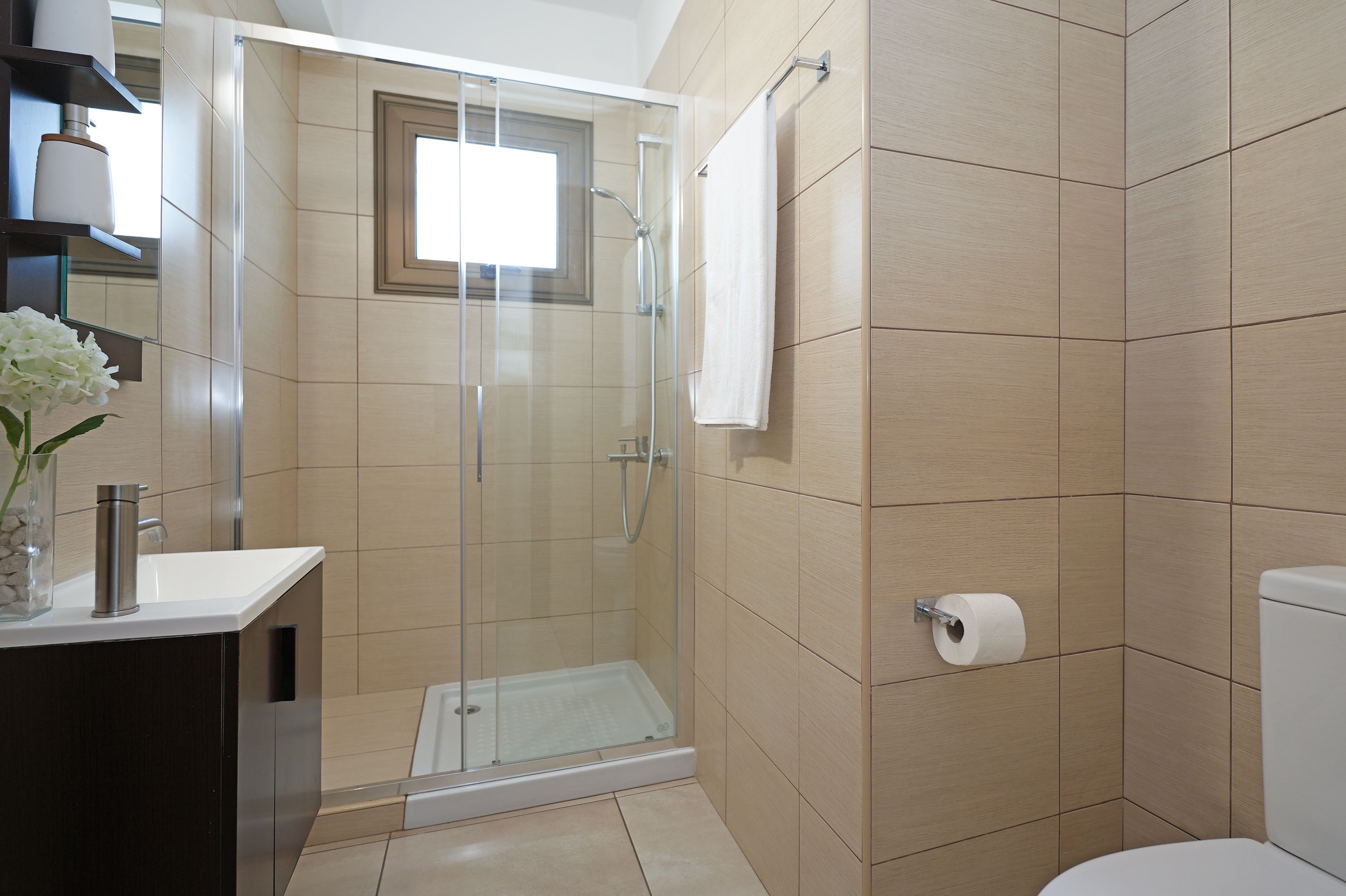 A modern bathroom with a glass-enclosed shower, a toilet, and a sink with a vase of flowers.
