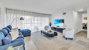 A modern living room with a blue sofa, a coffee table, a white armchair, and a flat-screen TV. - Rare Brickell Miami House - Walk to Nightlife / Dining / Shopping (Miami)
