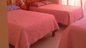 A room with two beds, a wooden headboard, a nightstand, a small table with a vase of flowers, and a window with curtains. - Hotel Ricarda Yopes (Acapulco)
