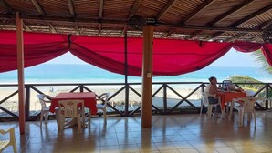 A covered outdoor seating area with tables and chairs, overlooking a beach. - Hotel Ricarda Yopes (Acapulco)