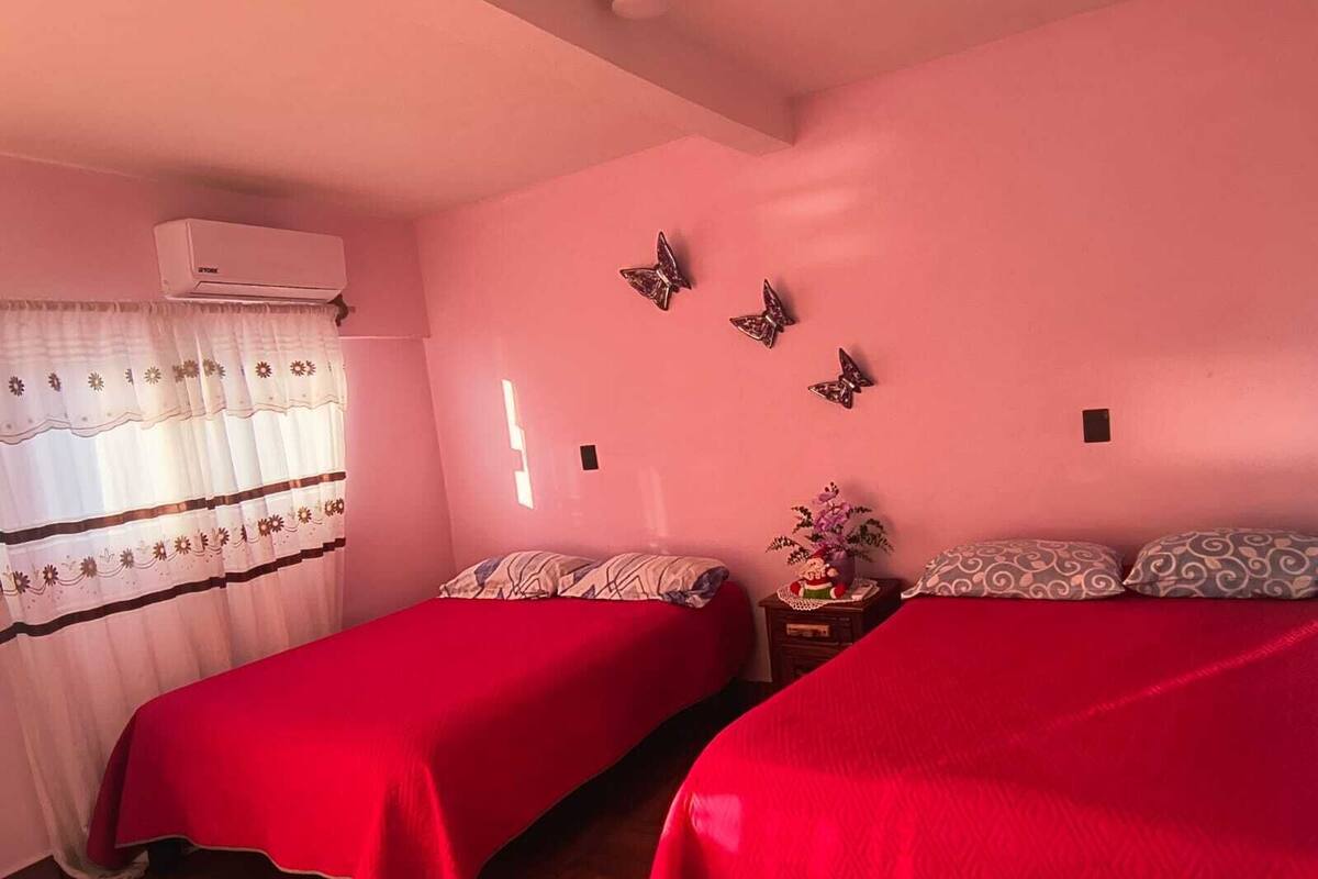 A room with two beds, a window with curtains, an air conditioning unit, and wall decorations.