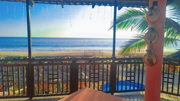 A beach view from a covered area with a pool and palm trees. - Hotel Ricarda Yopes (Acapulco)