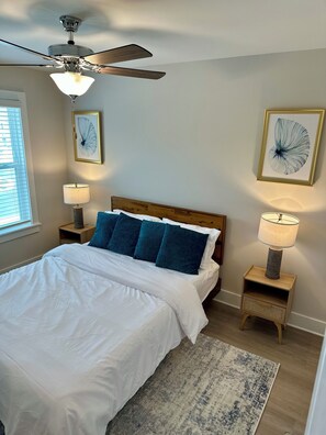 A bedroom with a bed, two bedside tables with lamps, a ceiling fan, and two wall-mounted artworks. - Beautiful 3-bedroom townhome with AC in Panama City. Refreshing take of Beach! (Panama City Beach)
