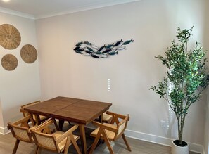 A dining area with a wooden table and four chairs, a wall-mounted decorative fish sculpture, and a potted plant. - Beautiful 3-bedroom townhome with AC in Panama City. Refreshing take of Beach! (Panama City Beach)