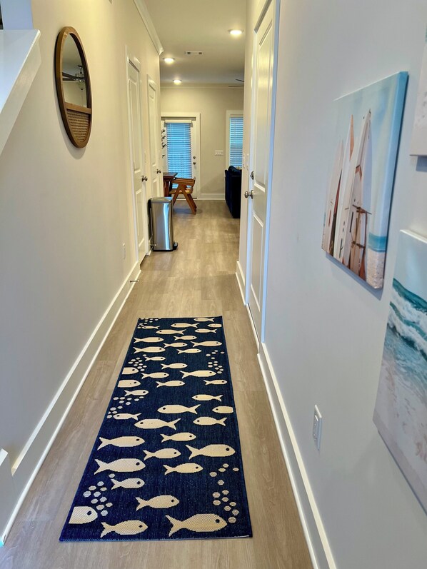 A hallway with a blue rug featuring fish patterns, white walls, and a door leading to a room with a window and a painting of sailboats. - Beautiful 3-bedroom townhome with AC in Panama City. Refreshing take of Beach! (Panama City Beach)