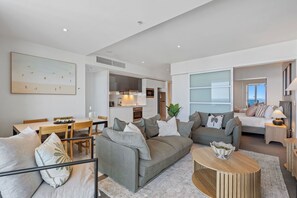 Ein modernes Wohnzimmer mit grauem Sofa, einem Esstisch und einer Küchenzeile.
