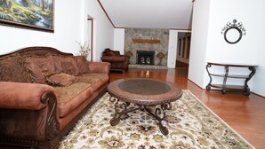 A living room with a brown sofa, a round coffee table, a patterned rug, a fireplace, and a stone wall.