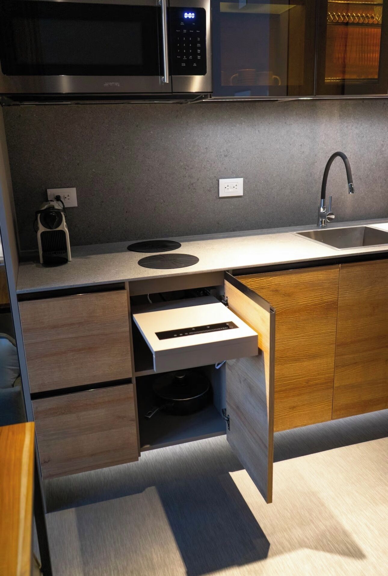 A modern kitchen with a microwave, a built-in oven, a sink, and a wooden cabinet.