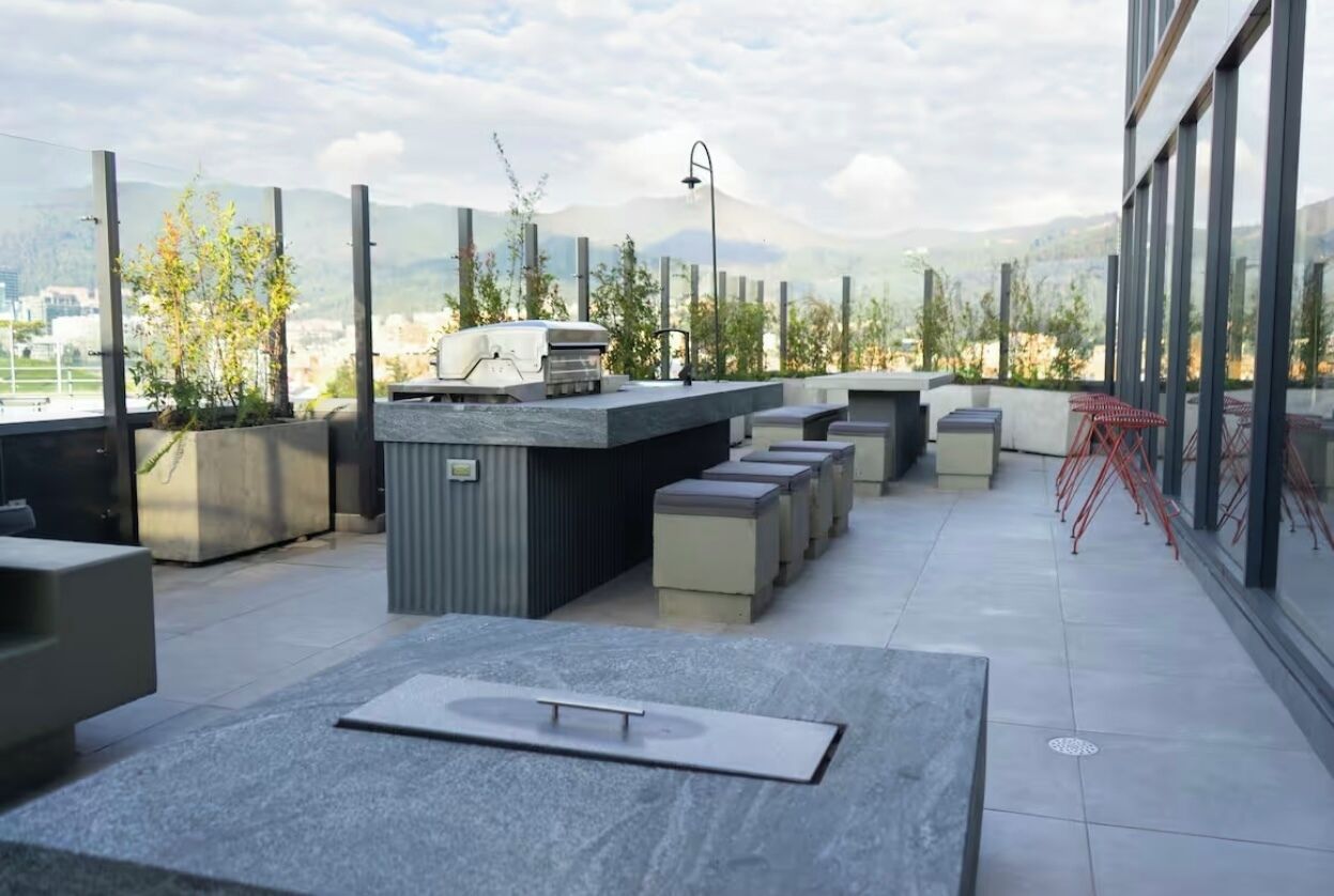 A rooftop terrace with outdoor seating, a grill, and a view of the city and mountains.