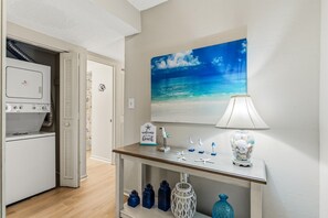 A laundry room with a washing machine, a drying rack, and a door leading to another room. - Beachfront Escape w/ Balcony, Pool, Tennis & Views (Destin)