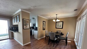 A dining area with a table and chairs, a kitchen in the background, and framed artwork on the walls. - A&C WATERFORD COTTAGE # 3 (Victoria)