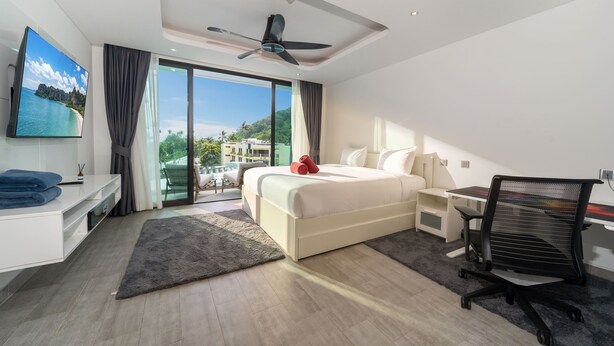 A modern hotel room with a bed, desk, chair, and a large window offering a view of the outdoors. - Absolute Twin Sands 5404 Private Pool (Patong)