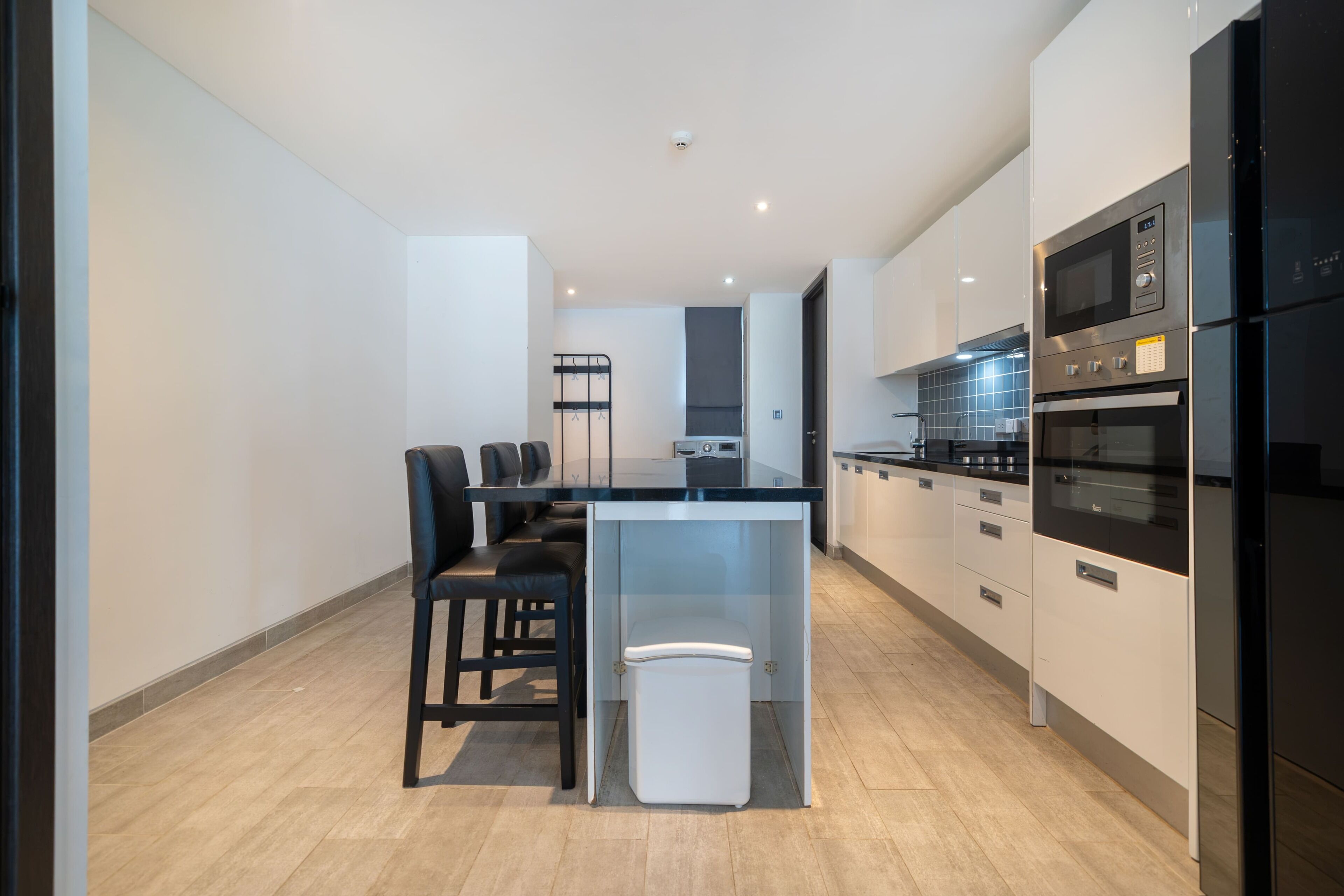Una cocina moderna con una isla central, taburetes negros y electrodomésticos integrados.