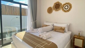Ein Schlafzimmer mit einem großen Bett, Meerblick durch eine Glastür und einem kleinen Nachttisch mit Lampe.
