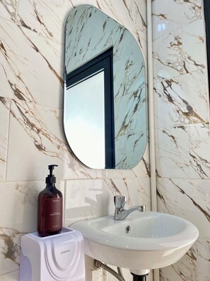 A bathroom with a marble-tiled wall, a white sink, a mirror, and a hand soap dispenser. - Villa Eclipse A1 (Jimbaran)