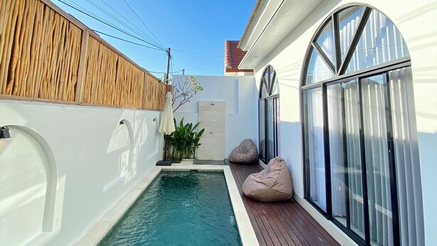 Ein moderner Poolbereich mit Holzterrasse, kleinem Pool und weißer Wand mit Fenster.