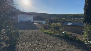 Ein Haus mit einem Schotterweg, einem kleinen Gartenhaus und einem Garten mit verschiedenen Pflanzen.