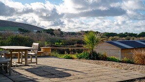 Eine Terrassengruppe mit Tisch und Stühlen, umgeben von einem Garten mit verschiedenen Pflanzen und einem Holzschuppen.
