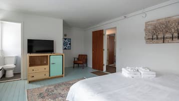 Un dormitorio con una cama, un televisor sobre un mueble de madera, una silla y un cuadro en la pared.