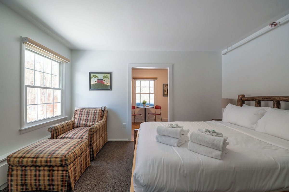 A hotel room with a large bed, a chair, a small table, and a window.