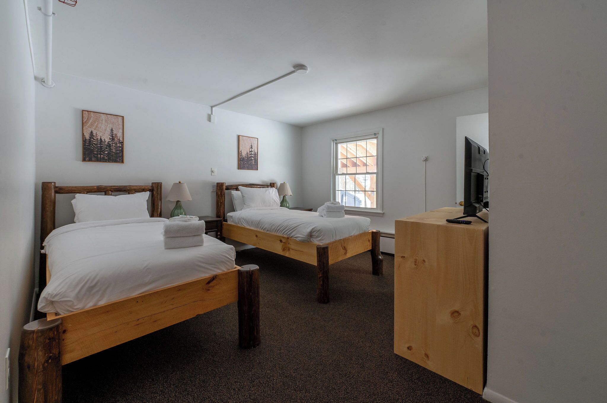 A room with two wooden beds, a desk, and a TV.