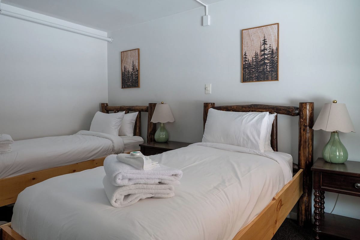 A hotel room with two single beds, each with a wooden headboard, white bedding, and a green vase on the nightstands.