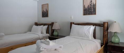 A hotel room with two single beds, each with a wooden headboard, white bedding, and a green vase on the nightstands.