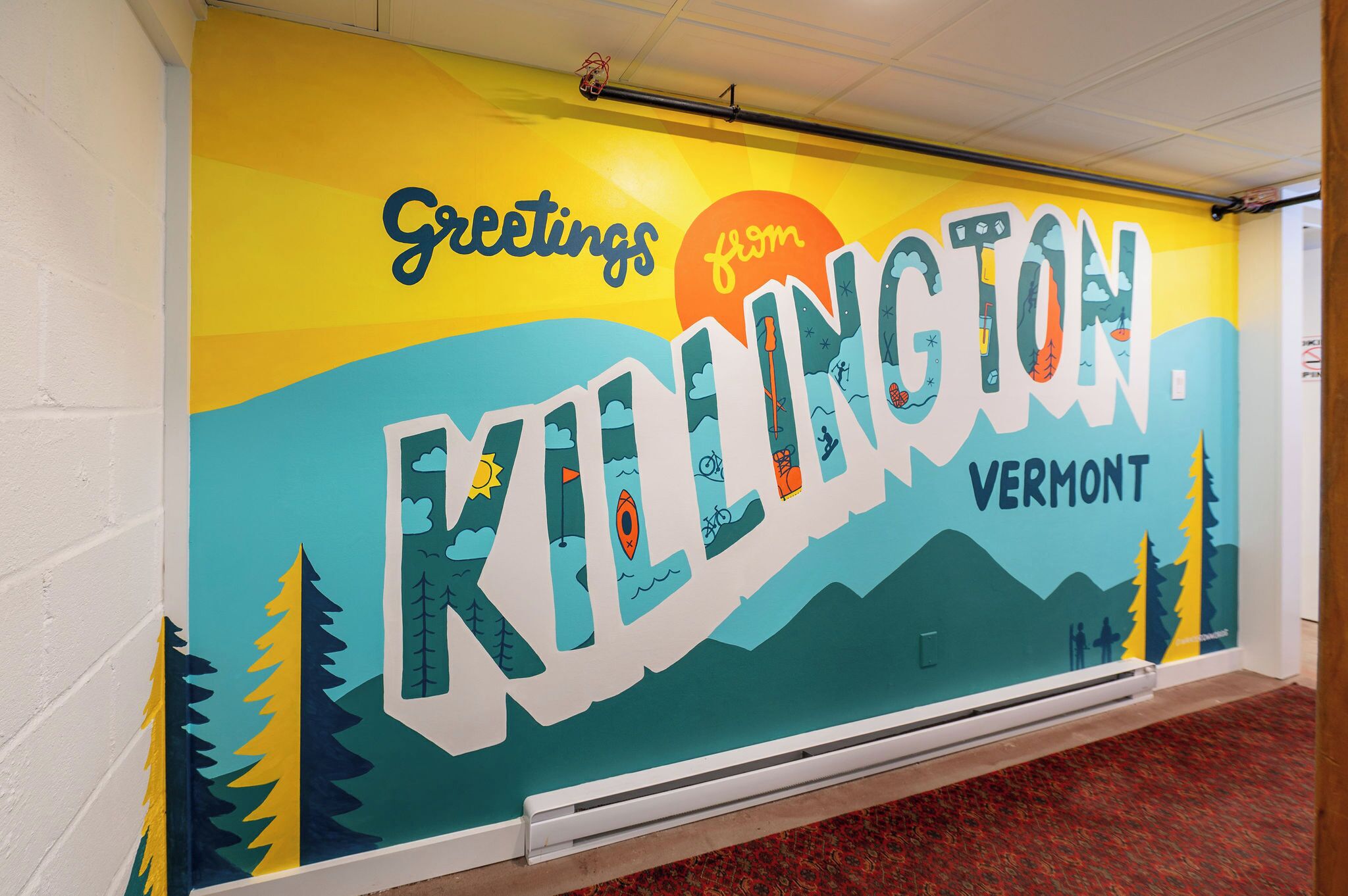 A wall mural with the text "Greetings from KILLINGTON, Vermont" and a scenic illustration of mountains, trees, and a sun.