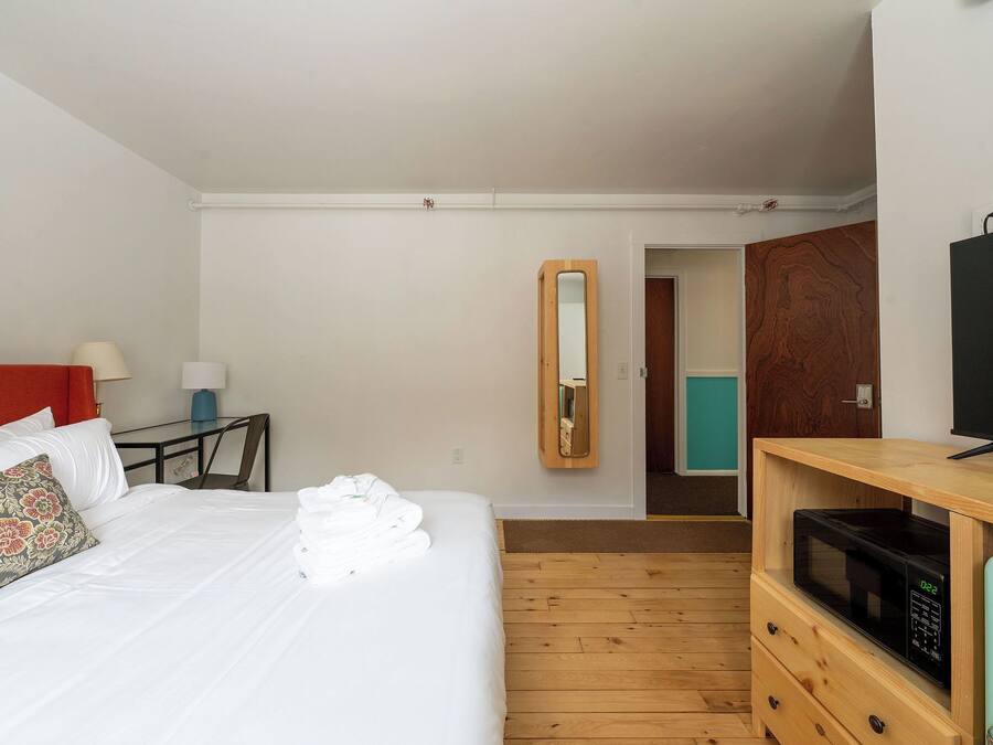 A hotel room with a bed, a desk, a mirror, a television, and a microwave.
