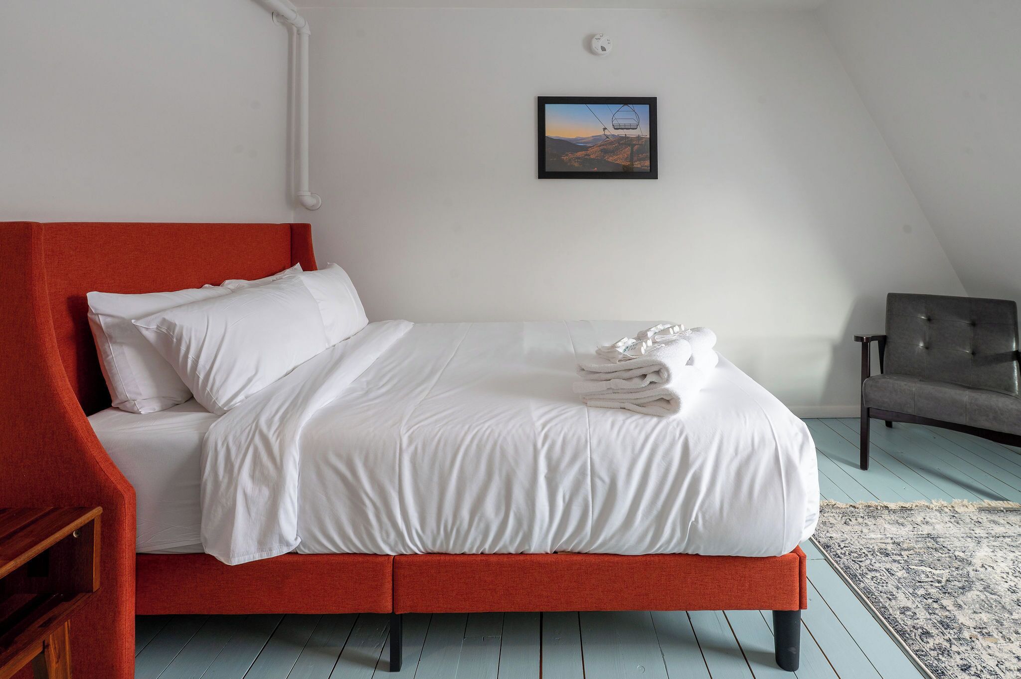 A neatly made bed with white linens, a red headboard, and a folded towel on the bed.