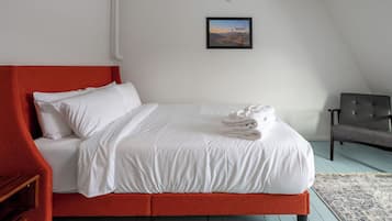 A neatly made bed with white linens, a red headboard, and a folded towel on the bed.